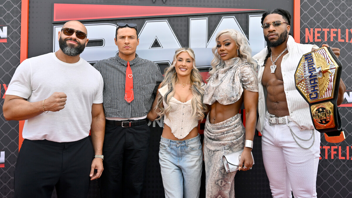 Rusev, Kit Wilson, Tiffany Stratton, Jade Cargill, and Trick Williams posing together on a red carpet at a WWE RAW event, with a branded backdrop. One person is holding an NXT Championship belt. The group is dressed in trendy and distinctive outfits.