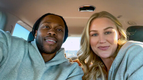 Dr Vic St John and Christine Hamilton sitting in the backseat of a car, smiling at the camera, wearing casual clothes in a well-lit, relaxed environment.