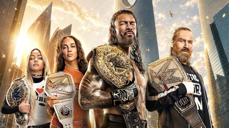 Four wrestling champions stand in a modern city with skyscrapers and a sunset sky, each holding championship belts, appearing strong and confident.