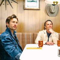 Glen Powell and Richard Linklater sit at a restaurant booth together.
