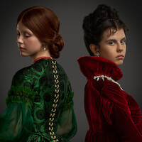 Duas mulheres em trajes de época, uma de verde e outra de vermelho, aparecem de costas uma para a outra diante de um fundo escuro. As expressões sérias e os figurinos elegantes criam uma atmosfera dramática e solene.