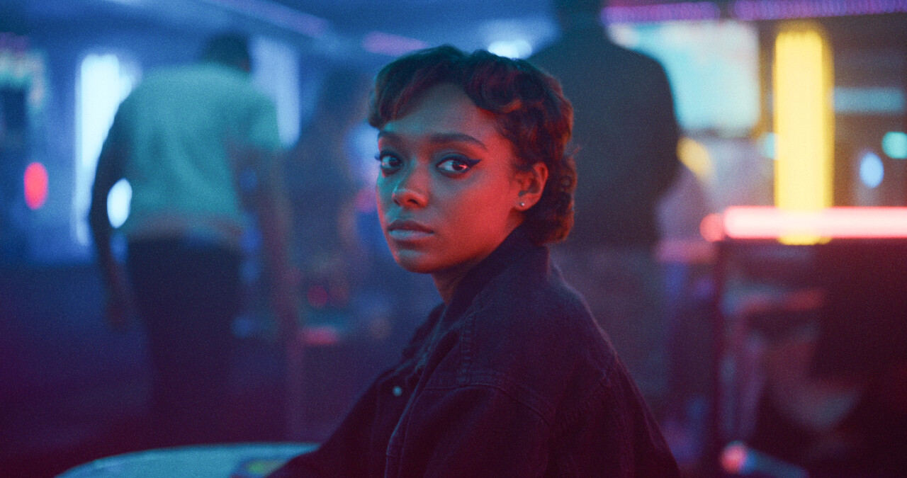 Sophie Wilde as Mia sits in a pub with blue and pink lights around her in Season 1 of 'Everything Now.'