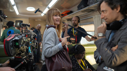 Film crew and actors on a busy train set, surrounded by cameras and equipment, with a focused yet lively atmosphere, suggesting a behind-the-scenes look at a movie production.