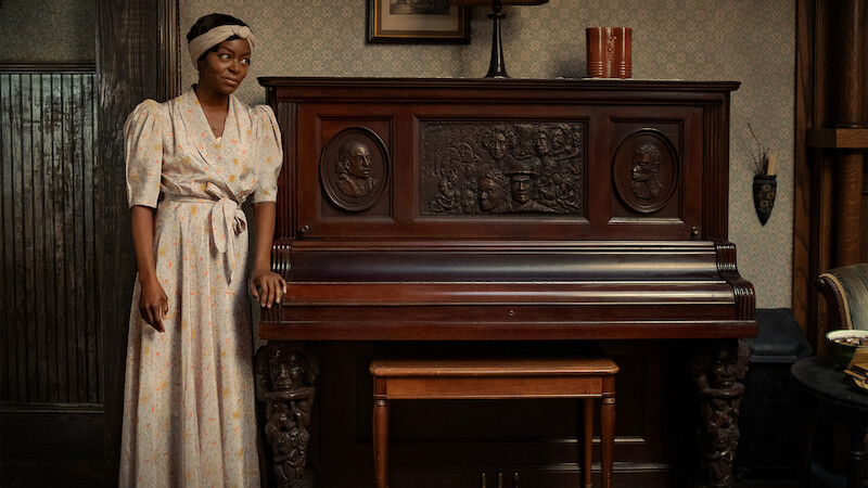 Berniece Charles (Danielle Deadwyler) stands in a white dress at an intricately carved wooden piano. 