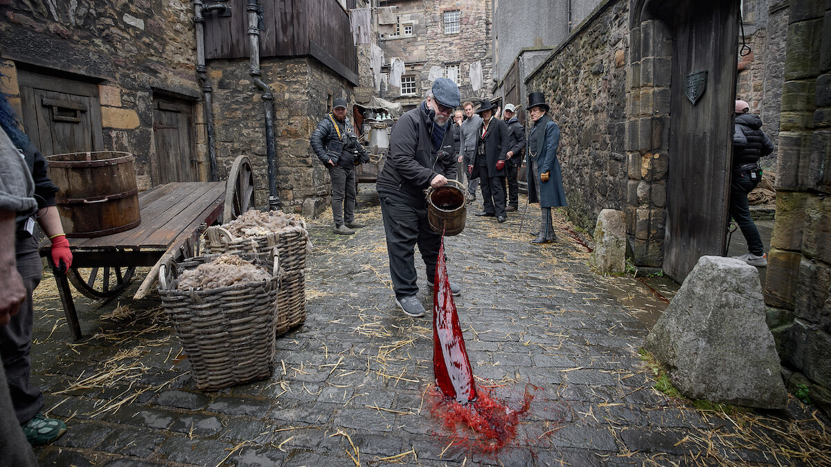 Guillermo del Toro throws a bucket of blood into cobblestoned streets on the set of Frankenstein.