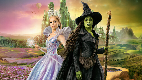 A magical fairy in a sparkling gown and a green-skinned witch with a pointed hat stand in a colorful fantasy landscape with a yellow brick road, flowers, and an emerald city in the background.